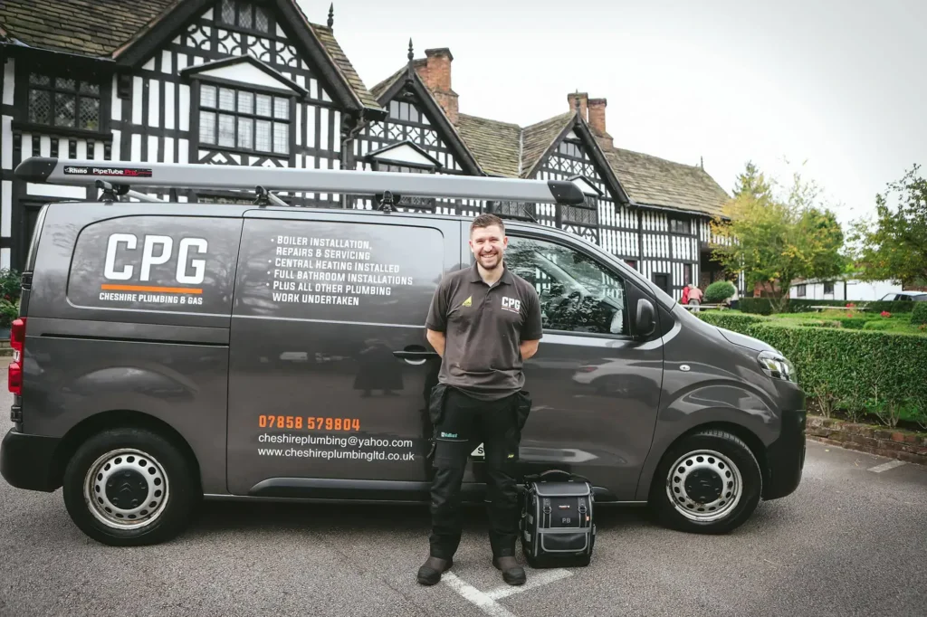 A CPG plumbers expert stands in front of a CPG-branded van, tool bag at his feet, outside a building with Tudor-style architecture in Cheshire.