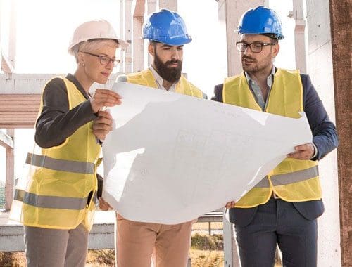 three men wearing a protective gears in a construction site looking at the blueprint
