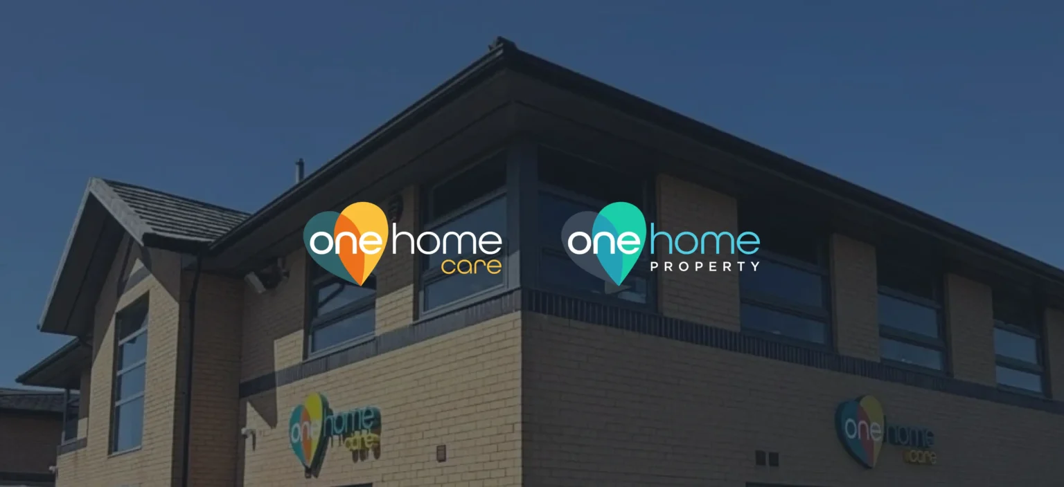 A modern brick building with corner windows displays two signs: "one home care" and "one home property," both featuring heart-shaped map pin logos, representing the trusted services of One Home Group.